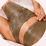 Persona sdraiata su un letto con indosso un impacco per il corpo verde scuro o una maschera per trattamenti termali.