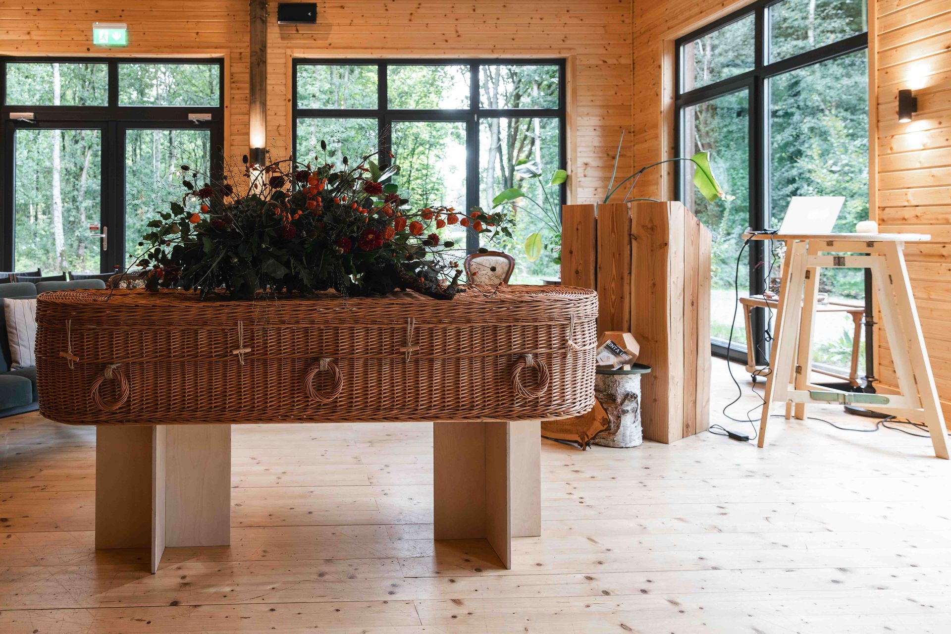 Een rieten plantenbak op een houten tafel in een lichte, rustieke kamer met grote ramen en een ladder.