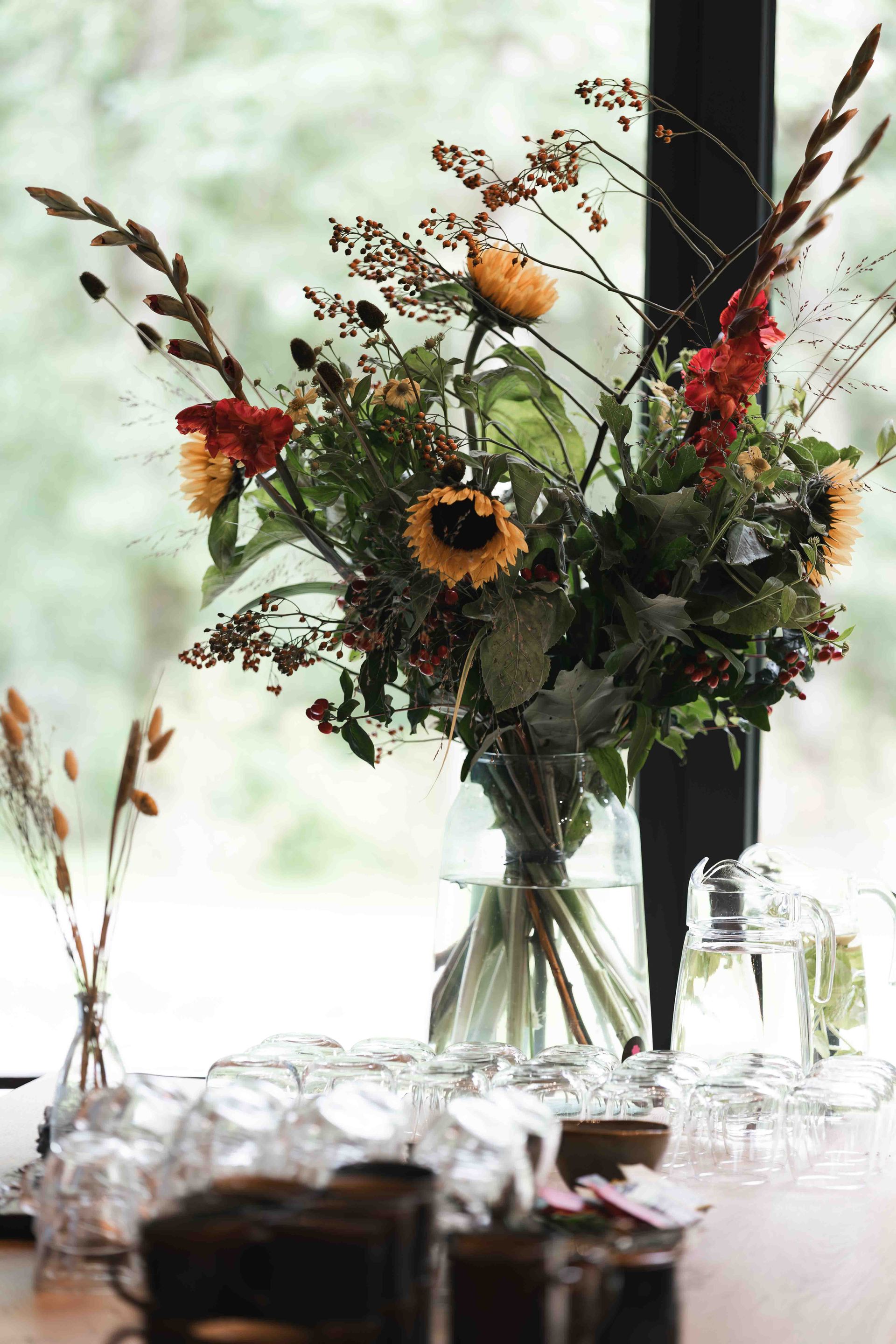 Bloemstuk met oranje en rode bloemen in een vaas op een tafel bij het raam.