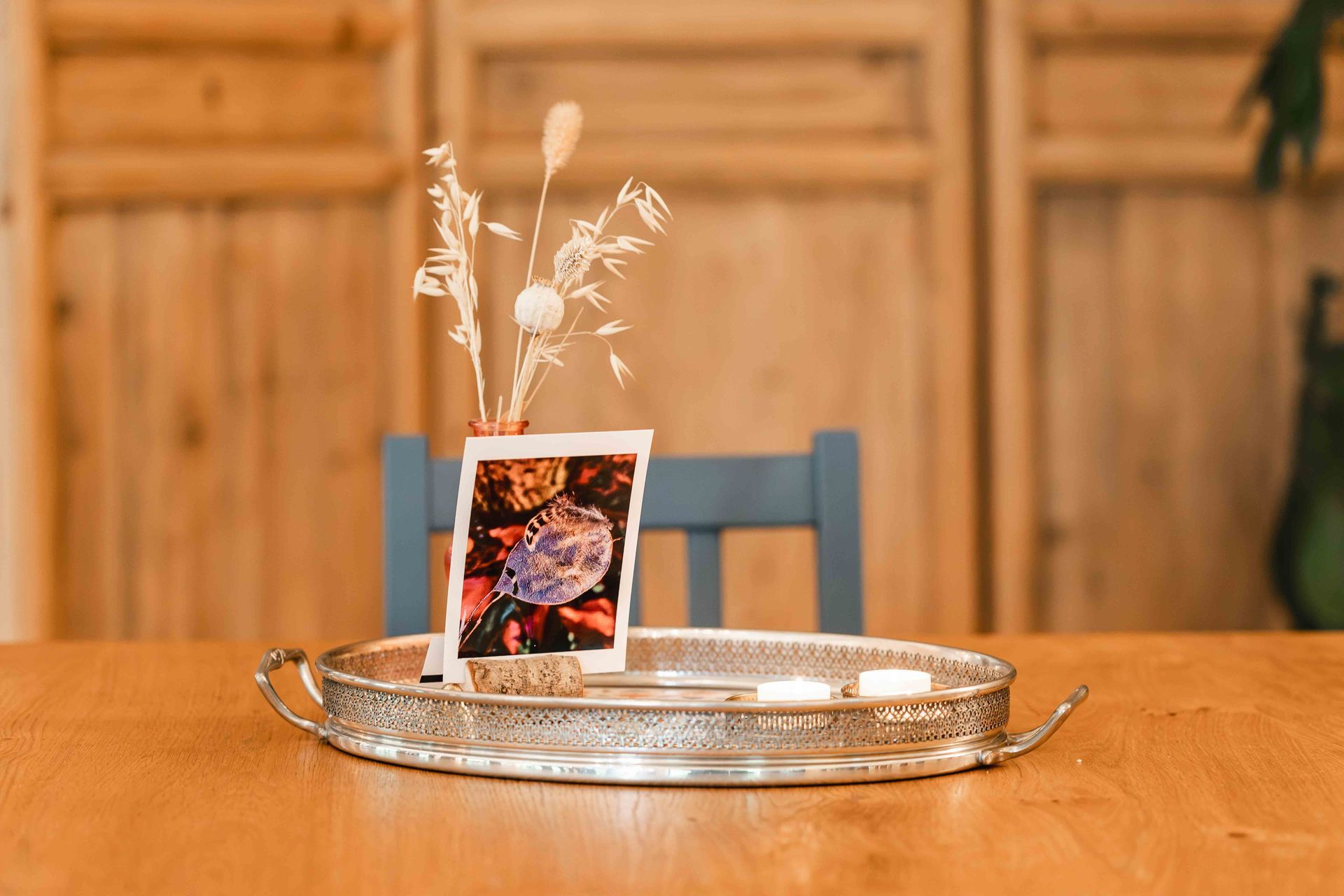 Decoratieve fotolijst op een zilveren dienblad met gedroogde bloemen op een houten tafel.