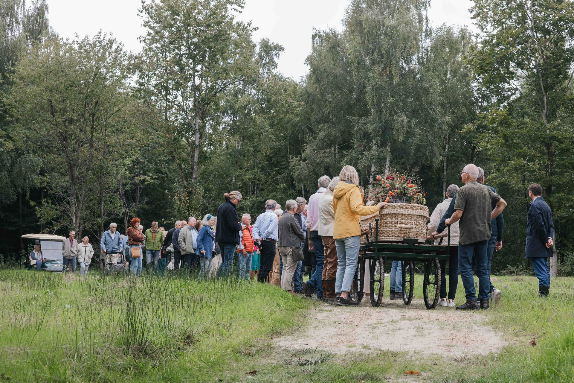 Mensen hadden zich buiten rond een picknicktafel verzameld, vlakbij een bospad, en stonden te praten.