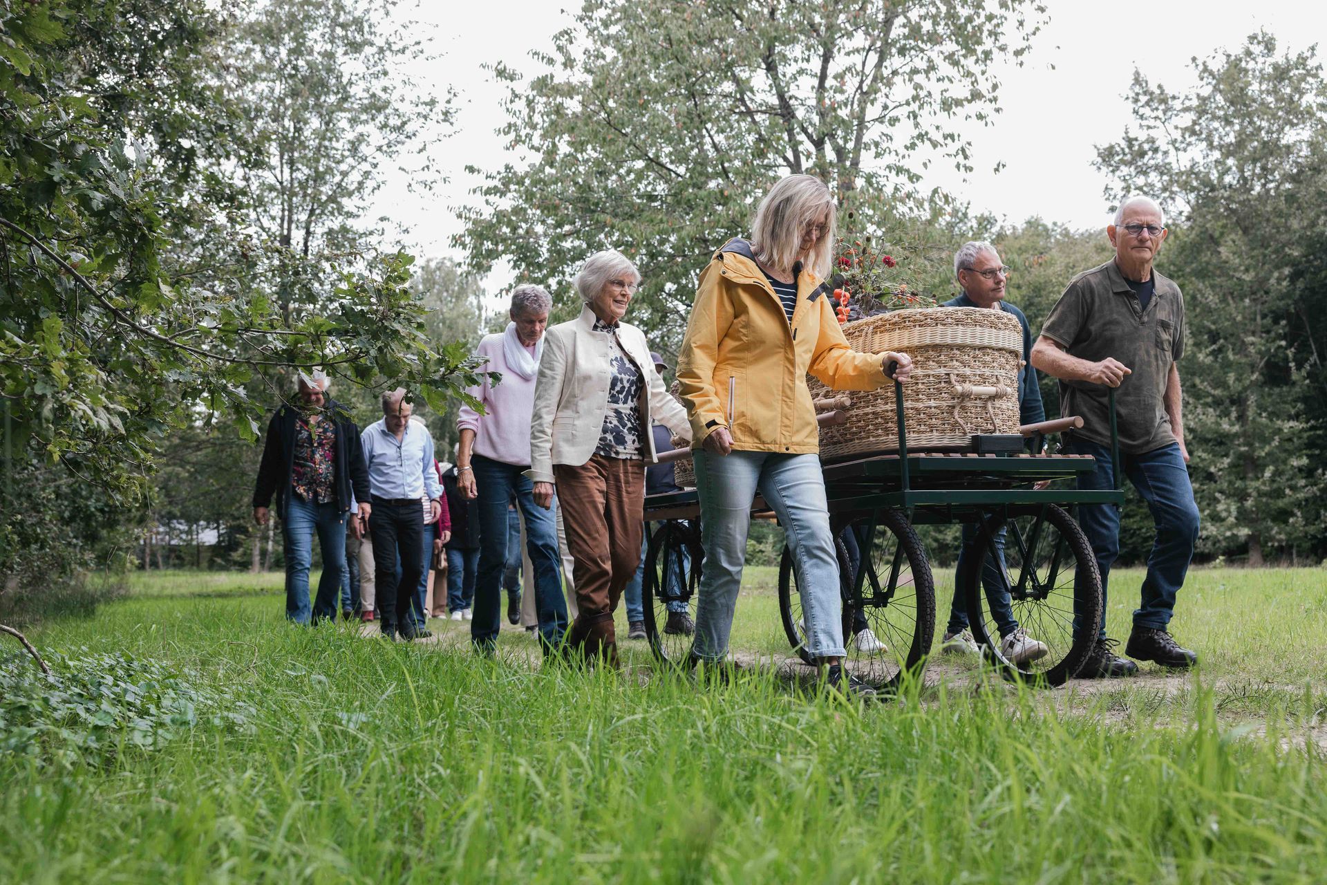 Mensen die buiten in een park wandelen en een kar met rieten manden voortduwen.
