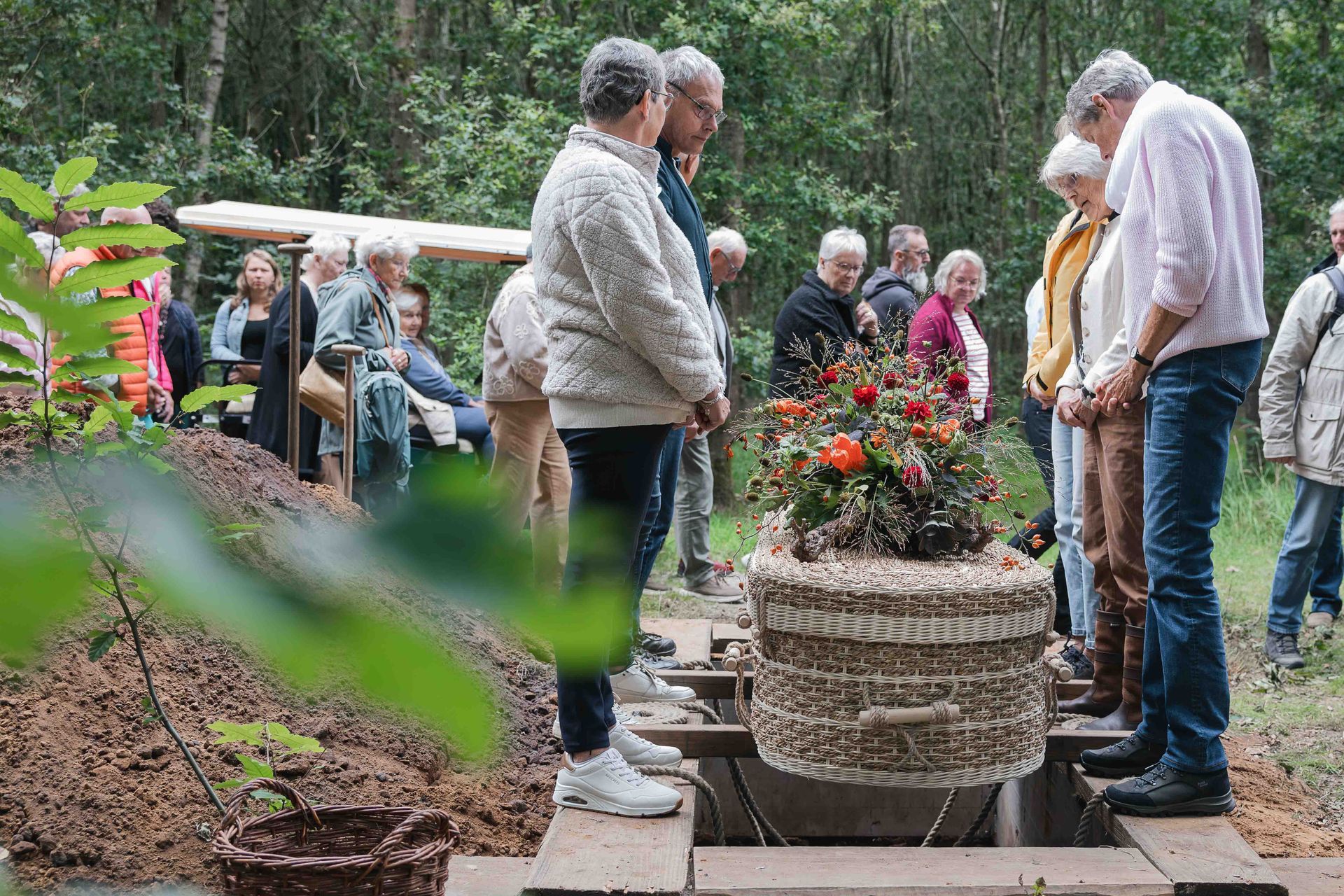 Mensen hadden zich verzameld rond bloembakken op een tuinpad, terwijl iemand in de open lucht een toespraak hield.