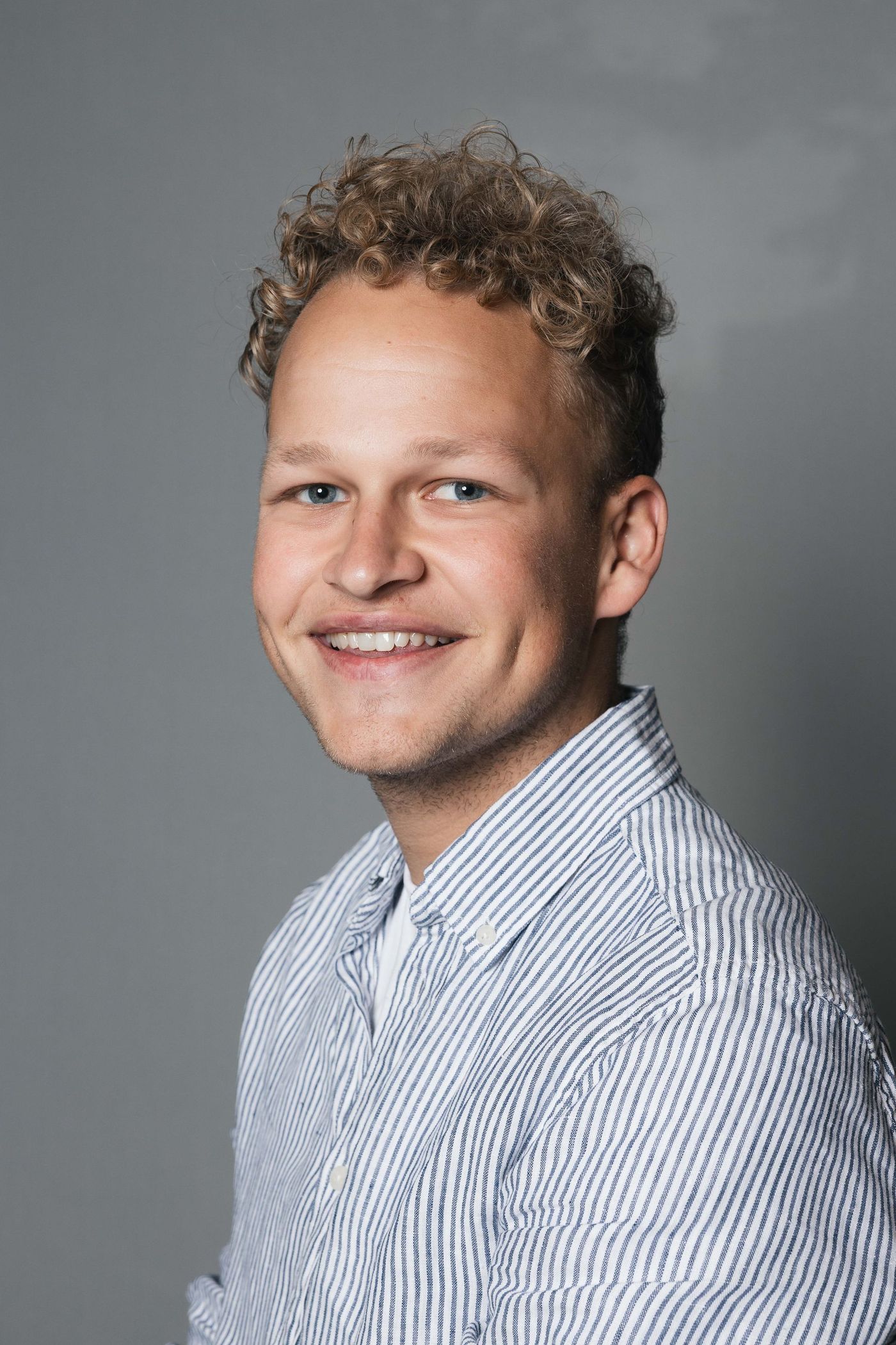 Glimlachende persoon in een blauw gestreept shirt tegen een grijze studioachtergrond geposeerd
