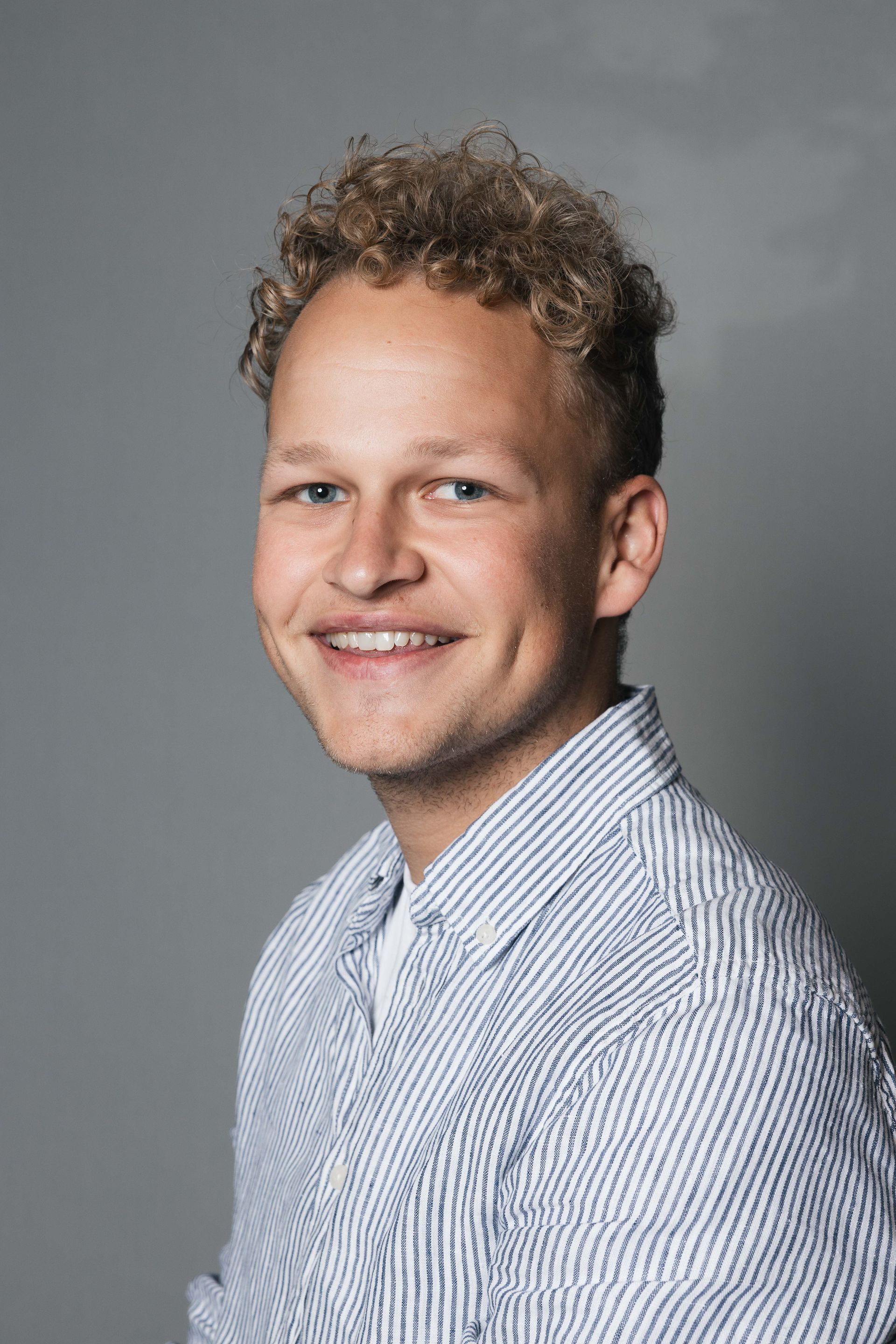 Glimlachend persoon in een gestreept shirt tegen een grijze studioachtergrond