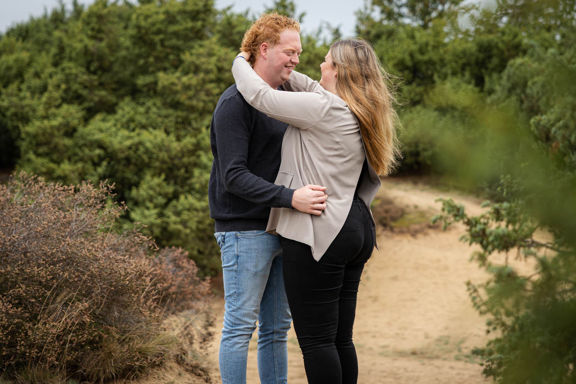 Een stel omhelst elkaar en lacht, buiten in een groene, natuurlijke omgeving.
