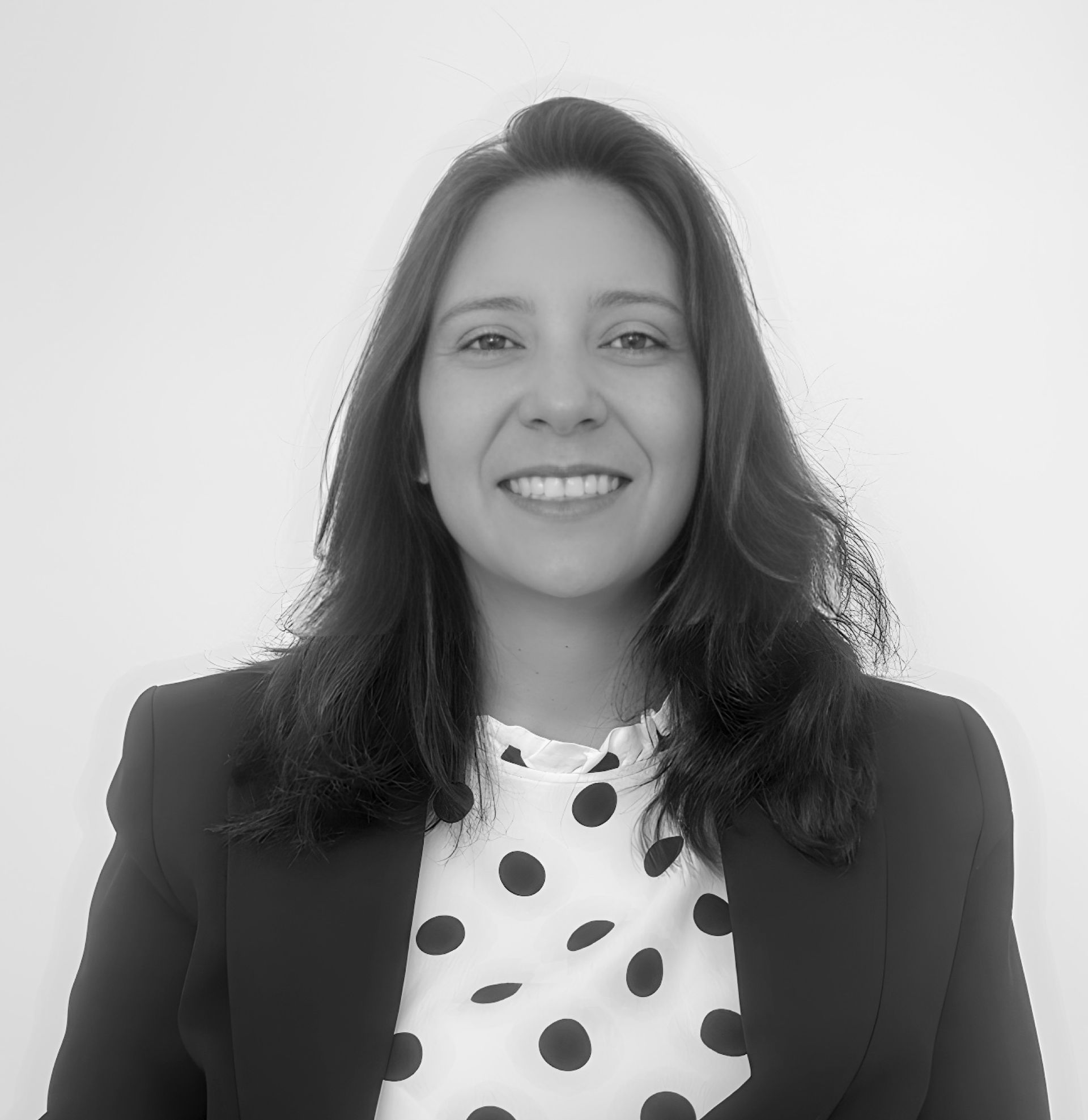A woman wearing a polka dot shirt and a black jacket is smiling in a black and white photo.