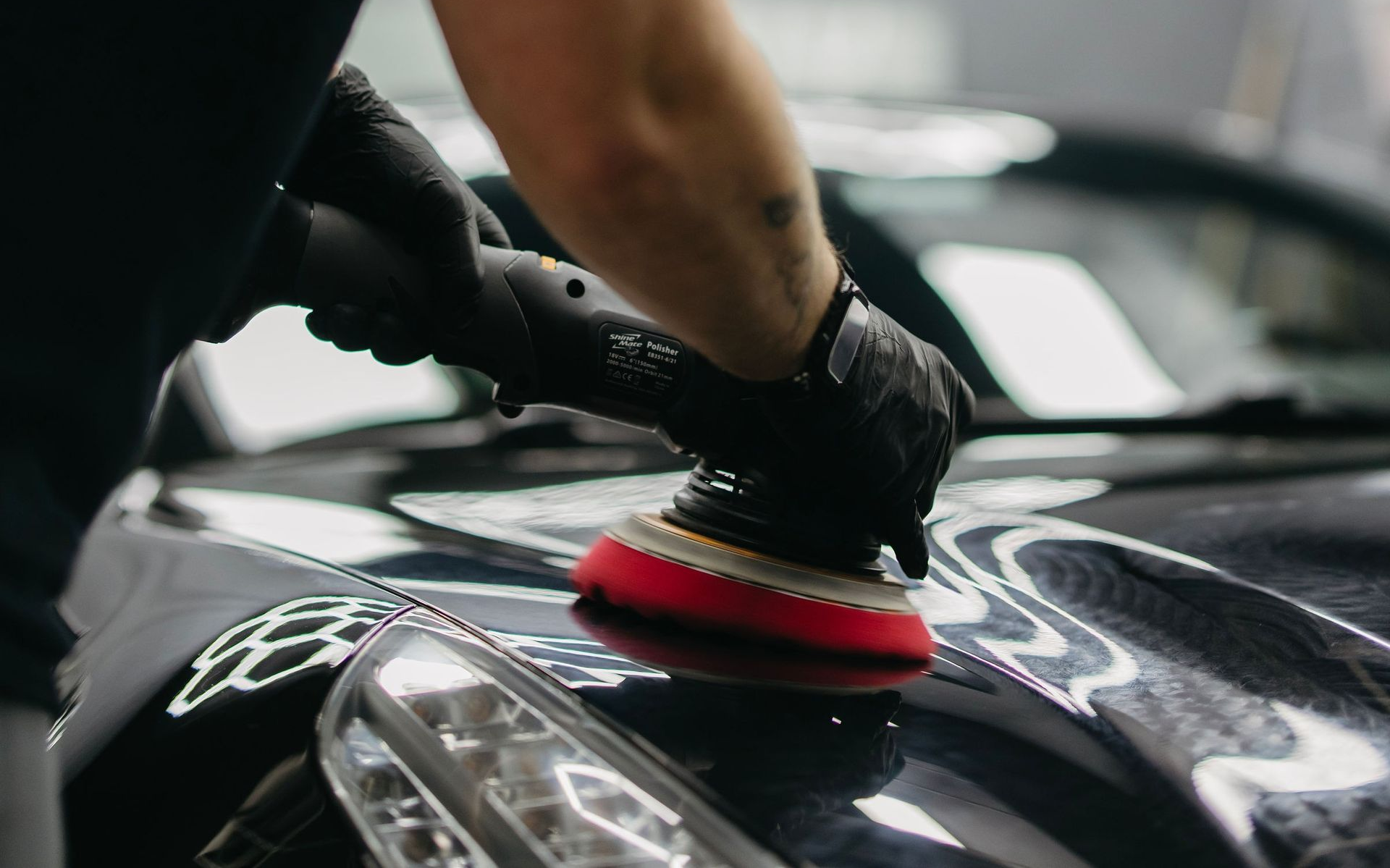 Person polishing a black car with a red buffer pad