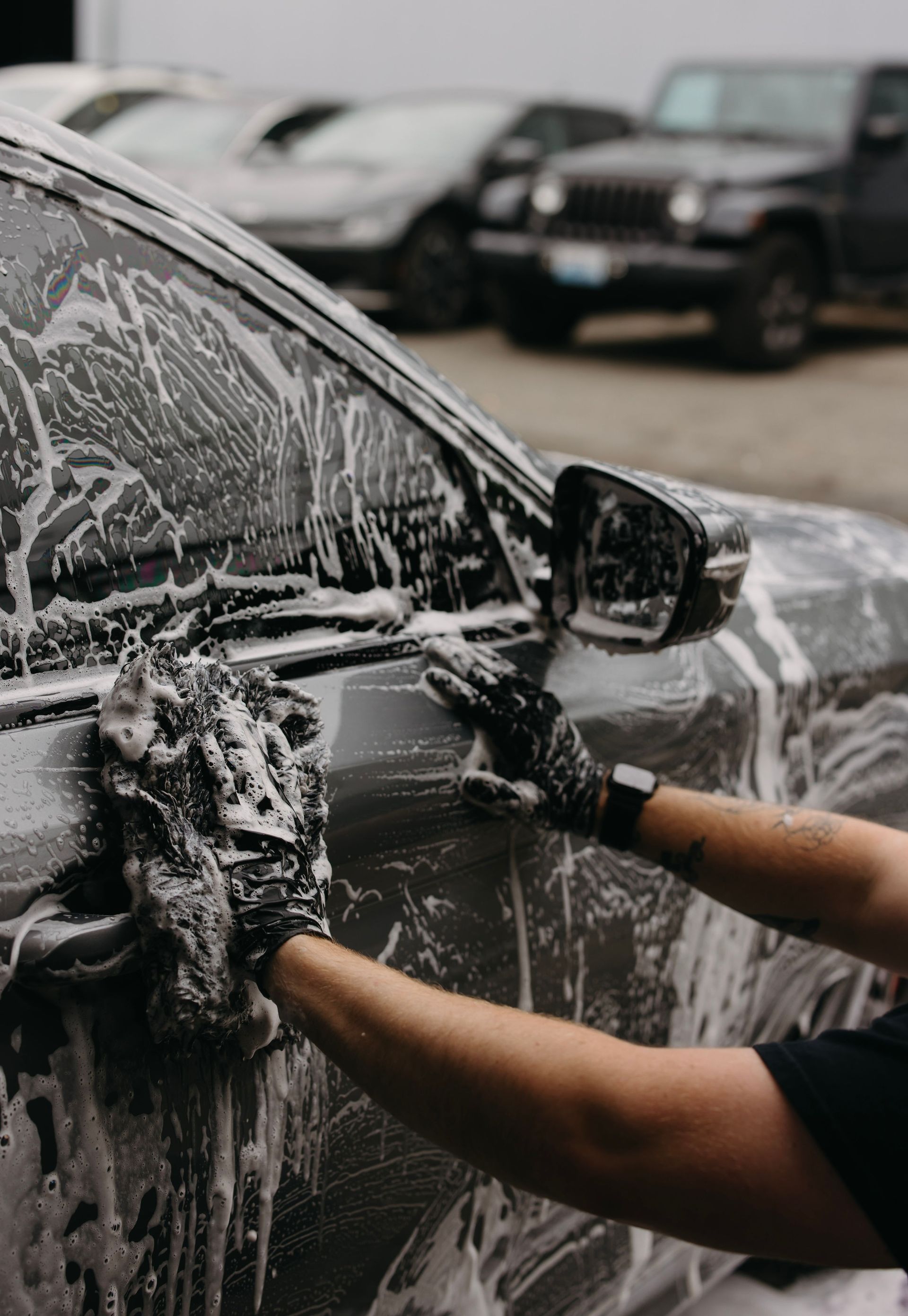 Person washing a black car with soapy foam in a car wash.