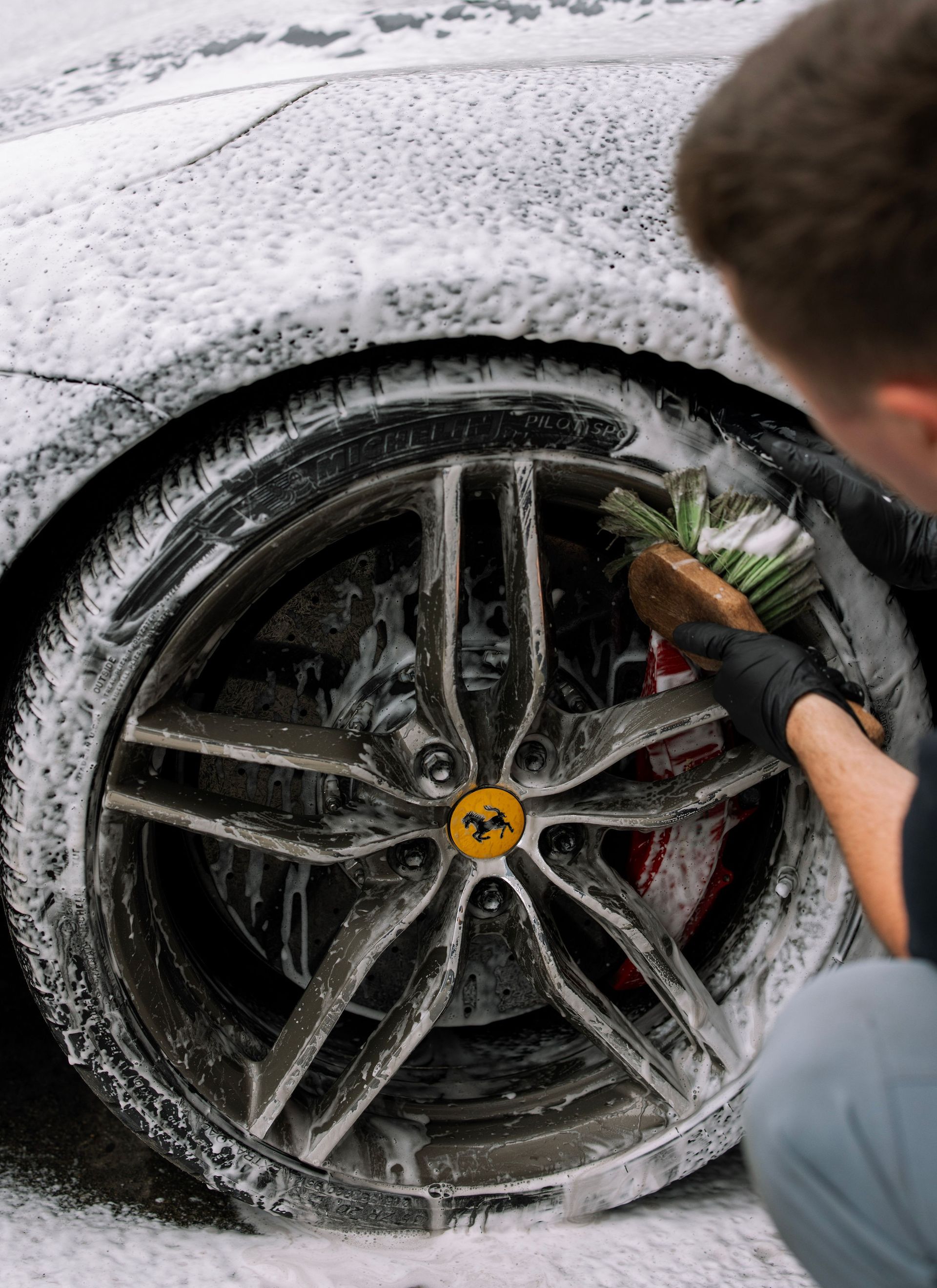 Person cleaning a snow-covered car wheel with a brush and water spray