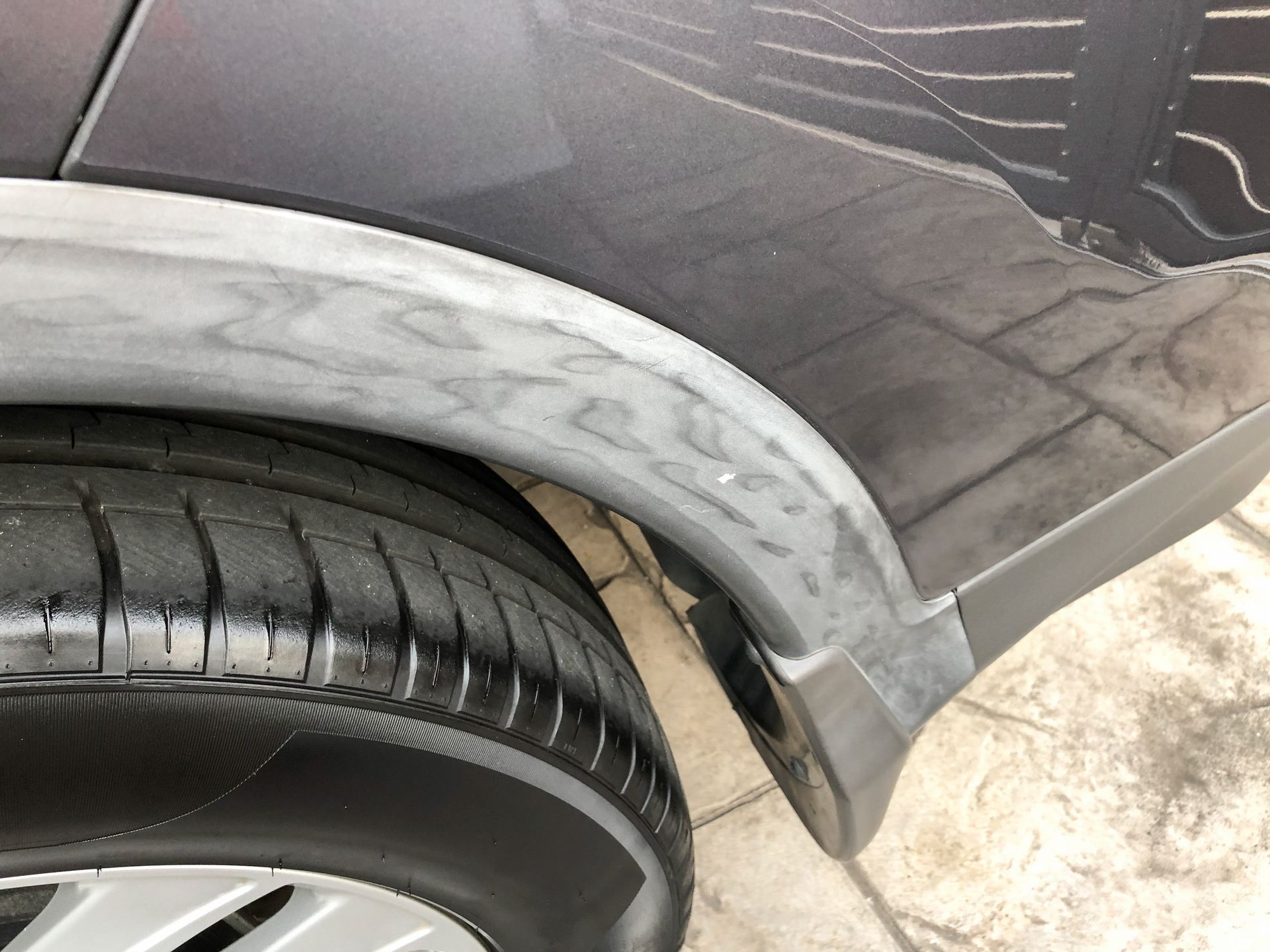 Close-up of a car’s rear wheel and fender with a gray scraped bumper panel