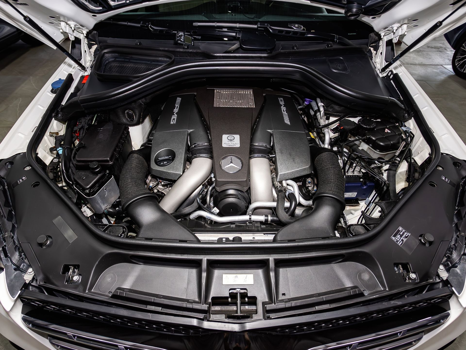 Open car hood showing a sleek black engine bay with twin engine covers and silver piping