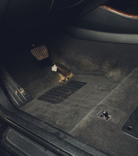 Car trunk floor with a small floor mat, pedal-like part, and a loose bolt on dark carpet.