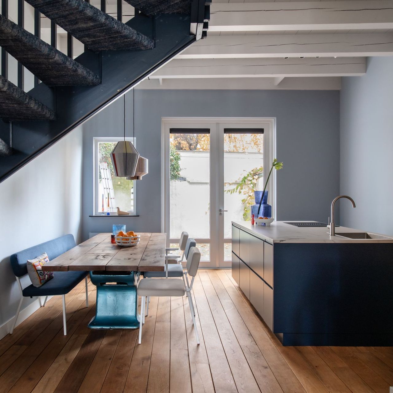 Keuken met houten vloer, donkerblauwe kasten, trap en eettafel.
