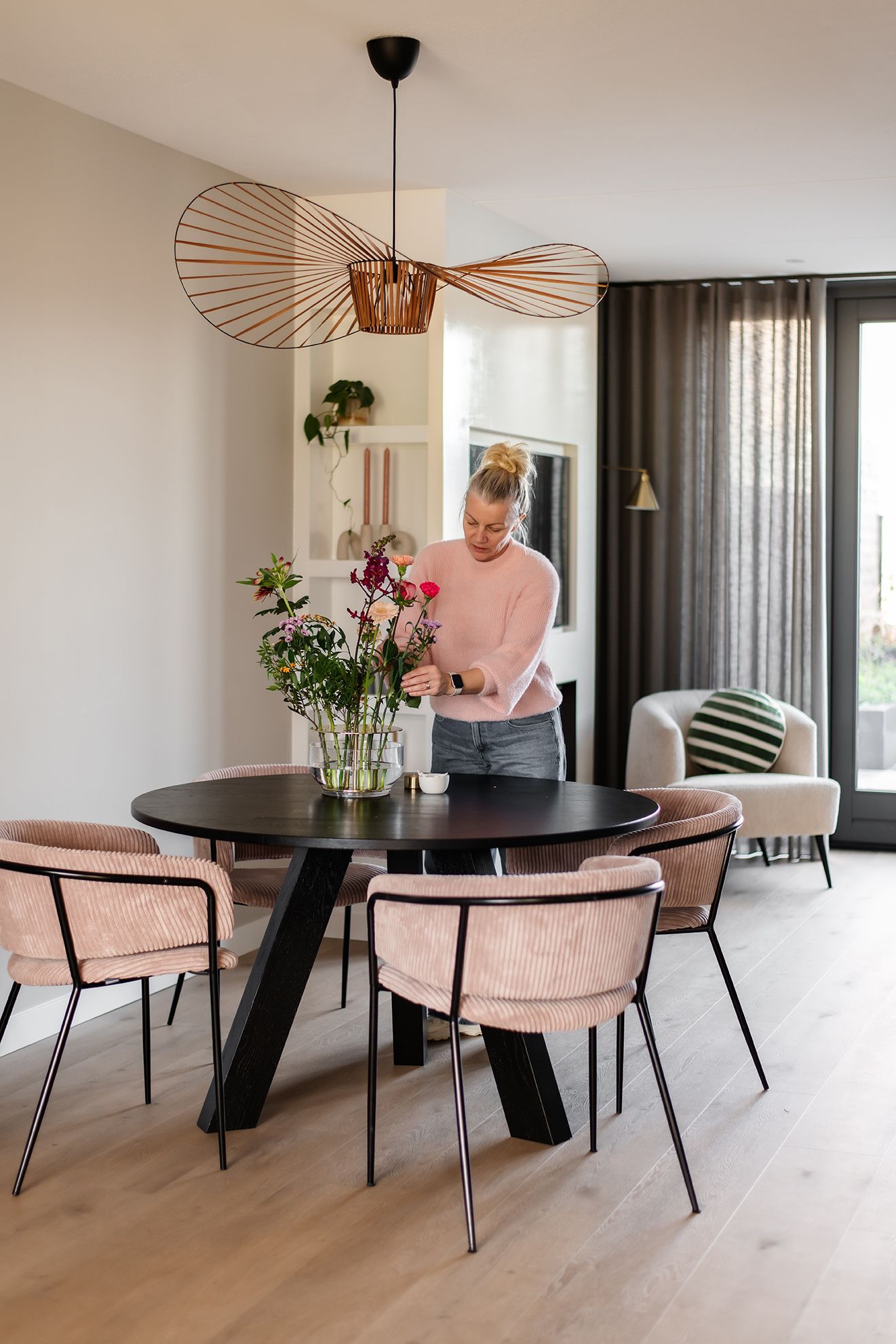 een vrouw schikt bloemen in een vaas in een eetkamer.