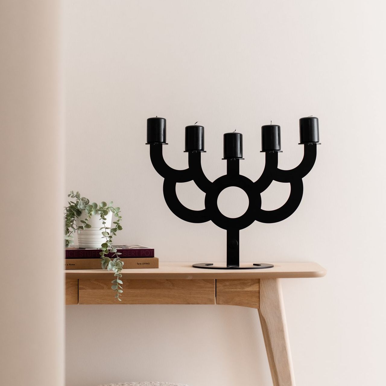 Zwarte kandelaar met vijf kaarsenhouders op een houten tafel, naast een kleine plant.