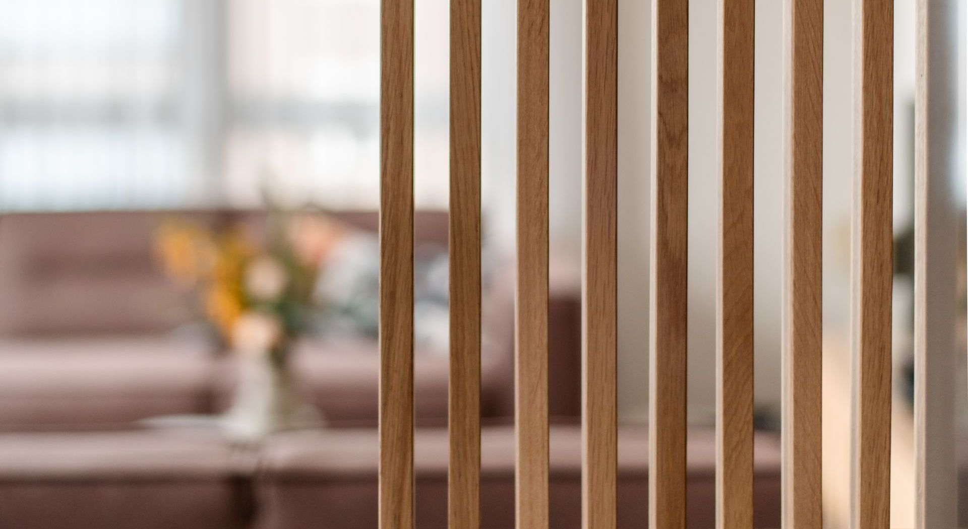 Houten scheidingswand voor een wazig tafereel in een woonkamer met een bank en bloemen.