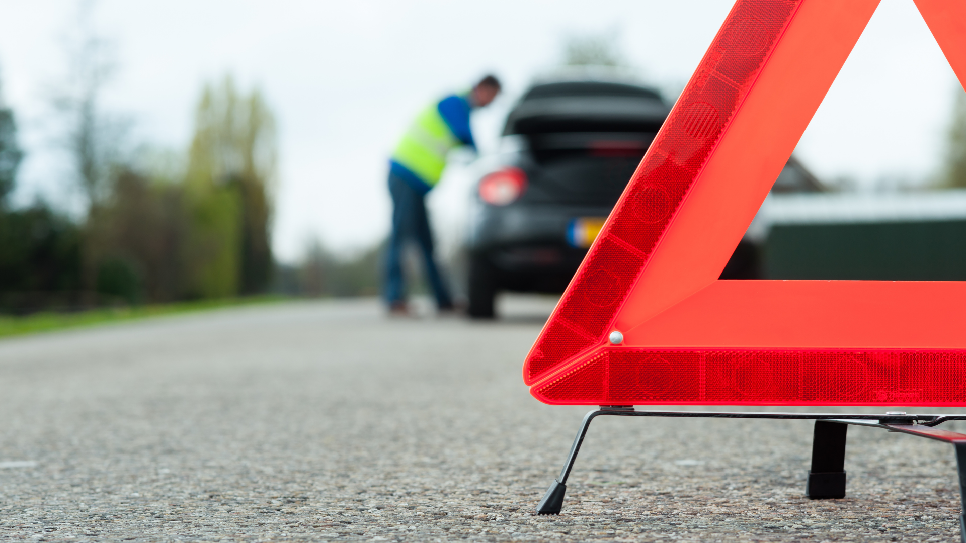 Red reflective warning triangle on road with person at a car.