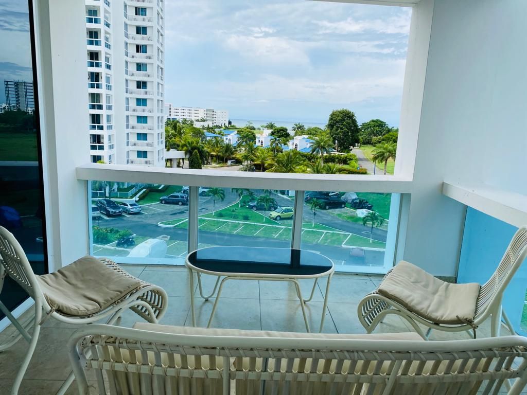 Balcony with two wicker chairs and a small table overlooking a beach and poolside view
