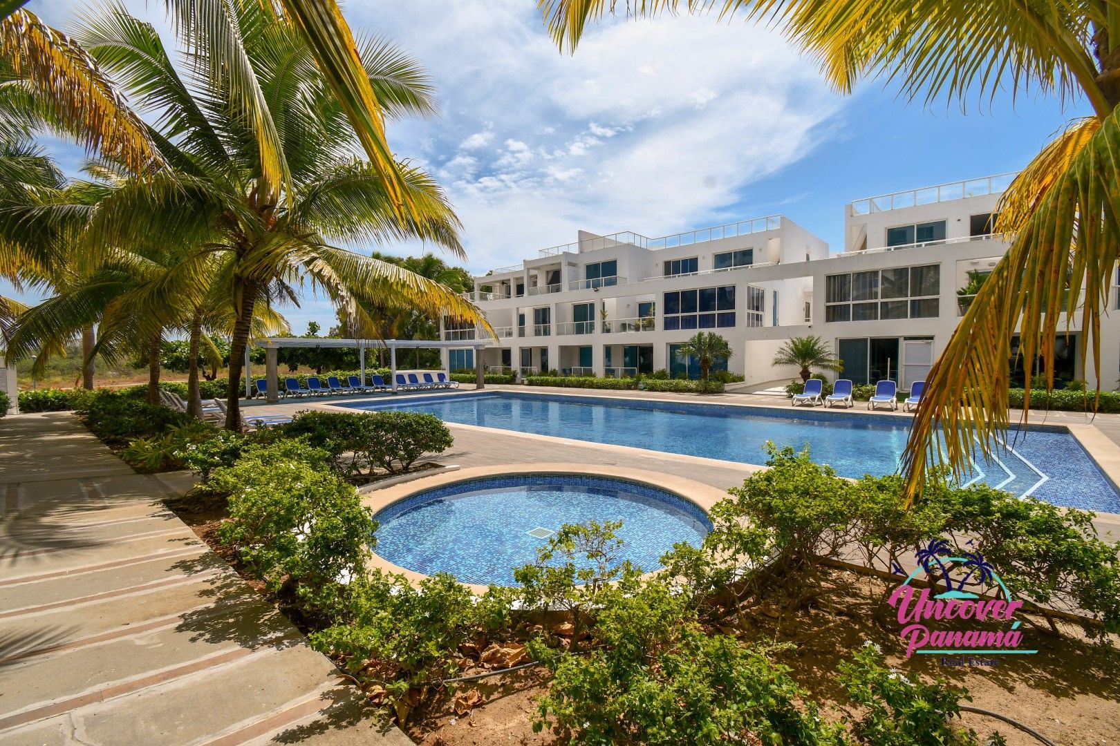 Palm-lined resort pool with blue water, white buildings, and sunny patio walkways