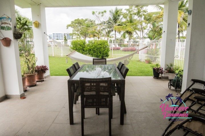 Covered patio with dining table and chairs, overlooking a green yard and hammock by a white fence.