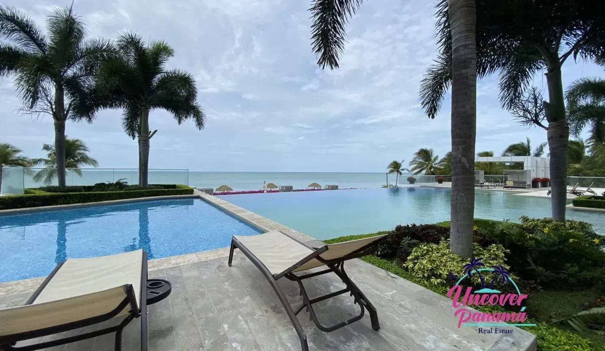 Infinity pool beside a tropical beach with palm trees, lounge chairs, and ocean view
