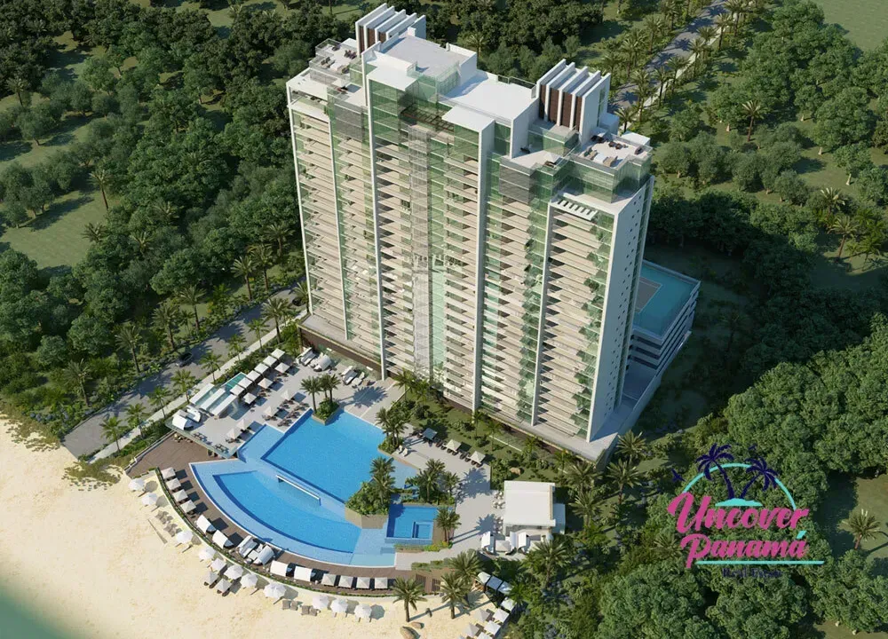 Aerial view of a tall residential tower with a blue swimming pool amid lush green trees.