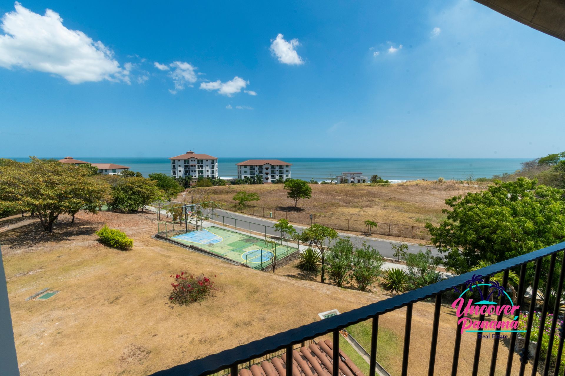 Balcony view of a sunny beachside resort with pool, palm trees, and ocean horizon