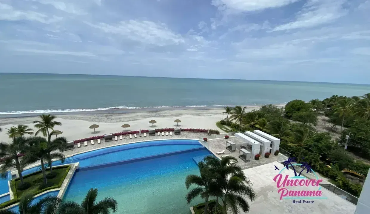 Beachfront resort pool overlooking a calm blue ocean under a partly cloudy sky