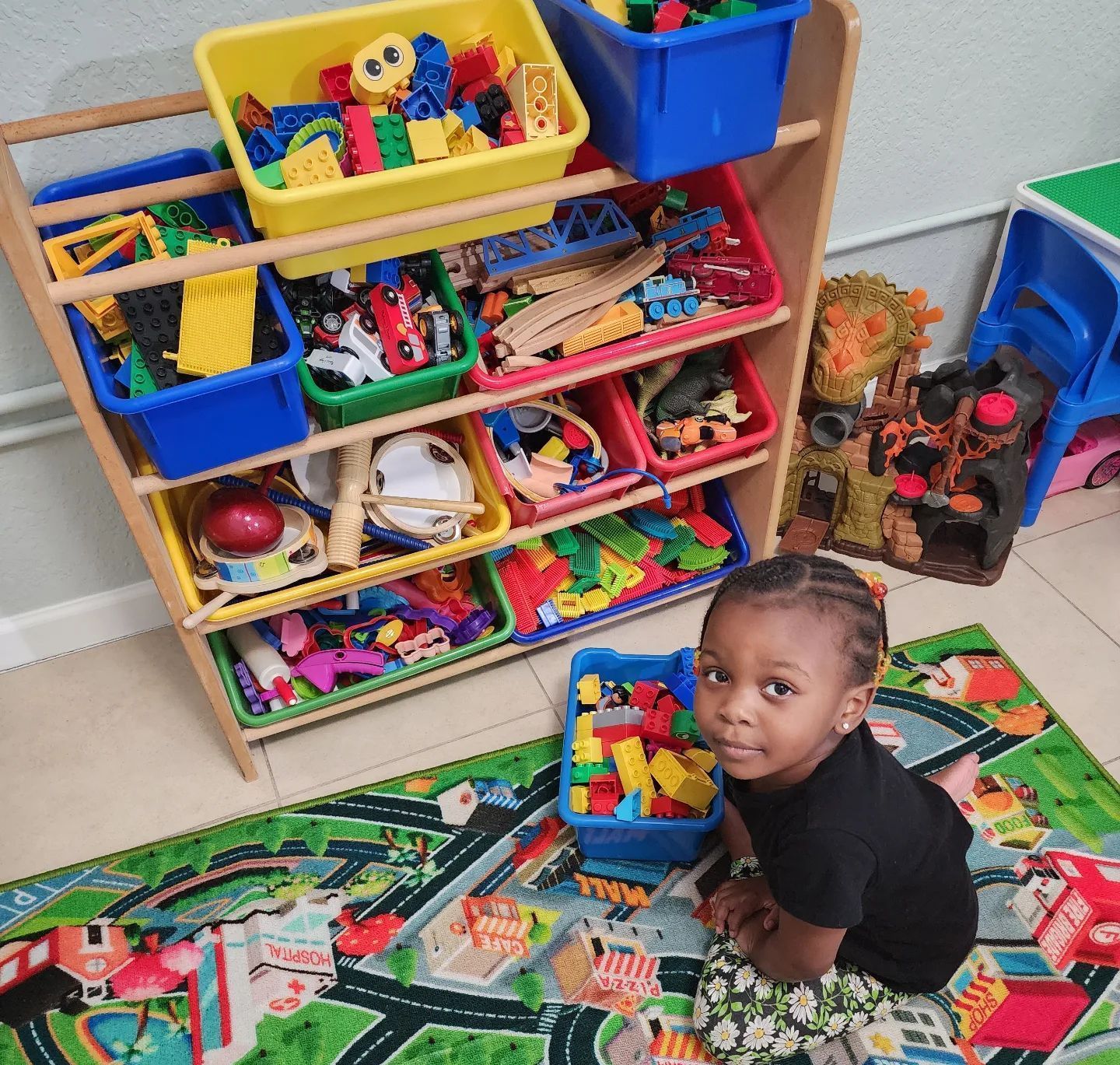 A little girl is sitting on a rug in front of a shelf full of toys.