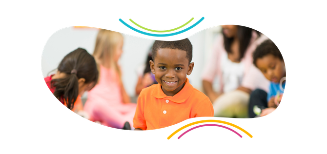 a young boy in an orange shirt is smiling in front of a group of children .