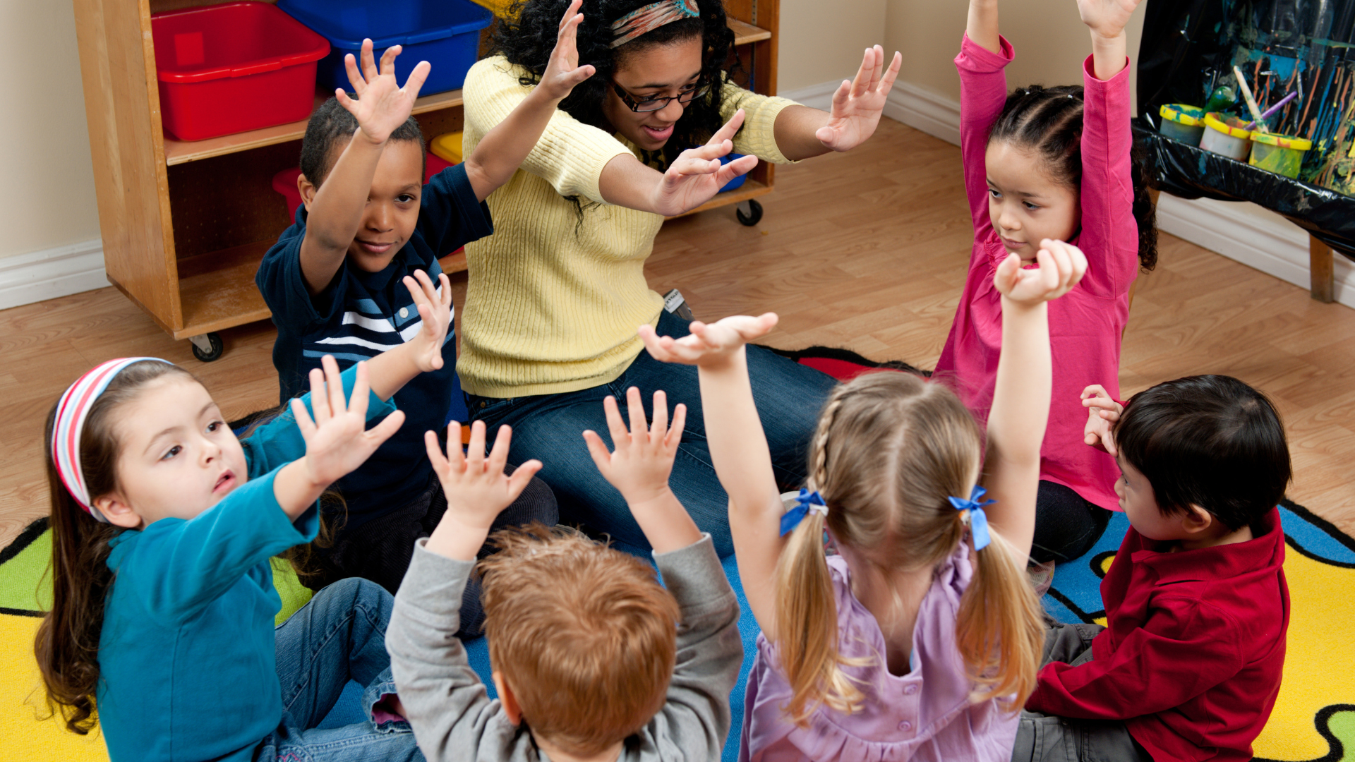 A group of children are sitting in a circle with their hands in the air.