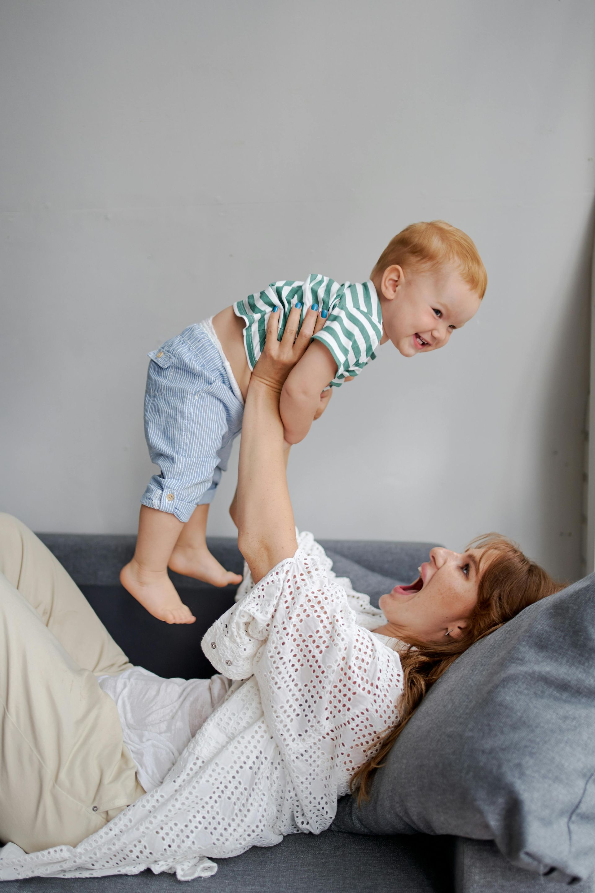 A woman is laying on a couch holding a baby in the air.