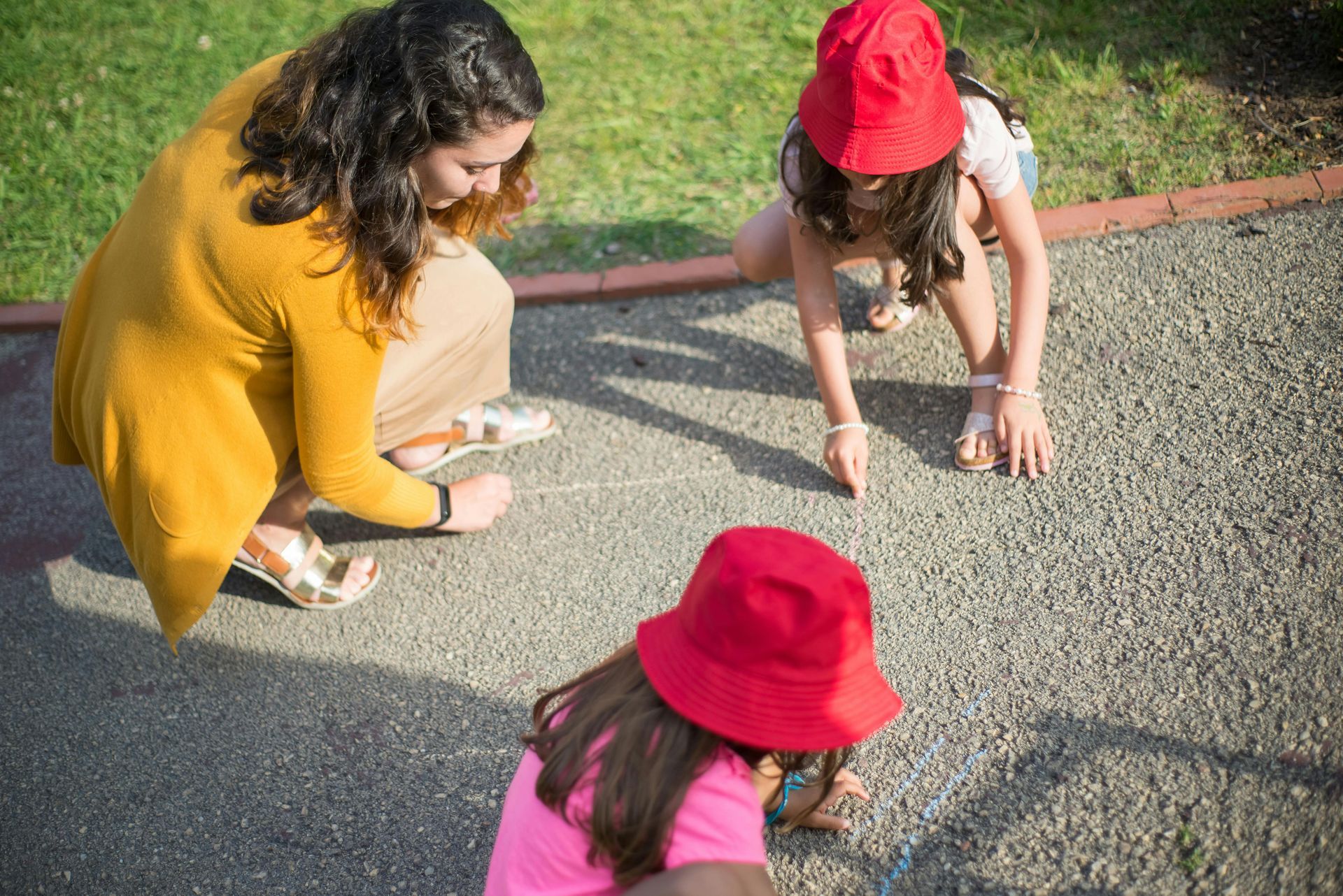A woman is kneeling down next to two little girls wearing red hats.