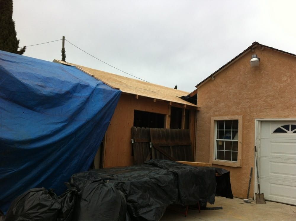 Backyard shed under repair, covered with blue tarp and black plastic beside a garage door