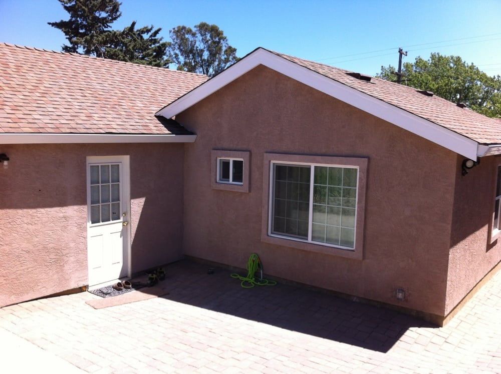 Back patio of a tan stucco house with white door, window, and sliding glass door under a tiled roof.