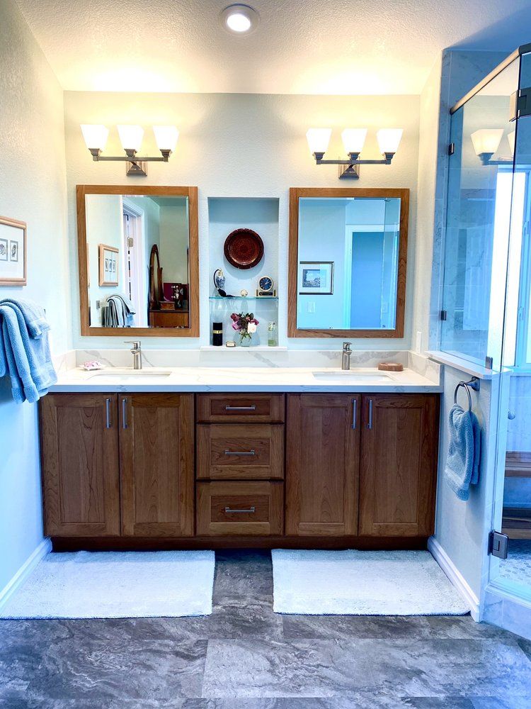 Bathroom vanity with double sinks, wooden cabinets, mirrors, and blue towels in a bright tiled room
