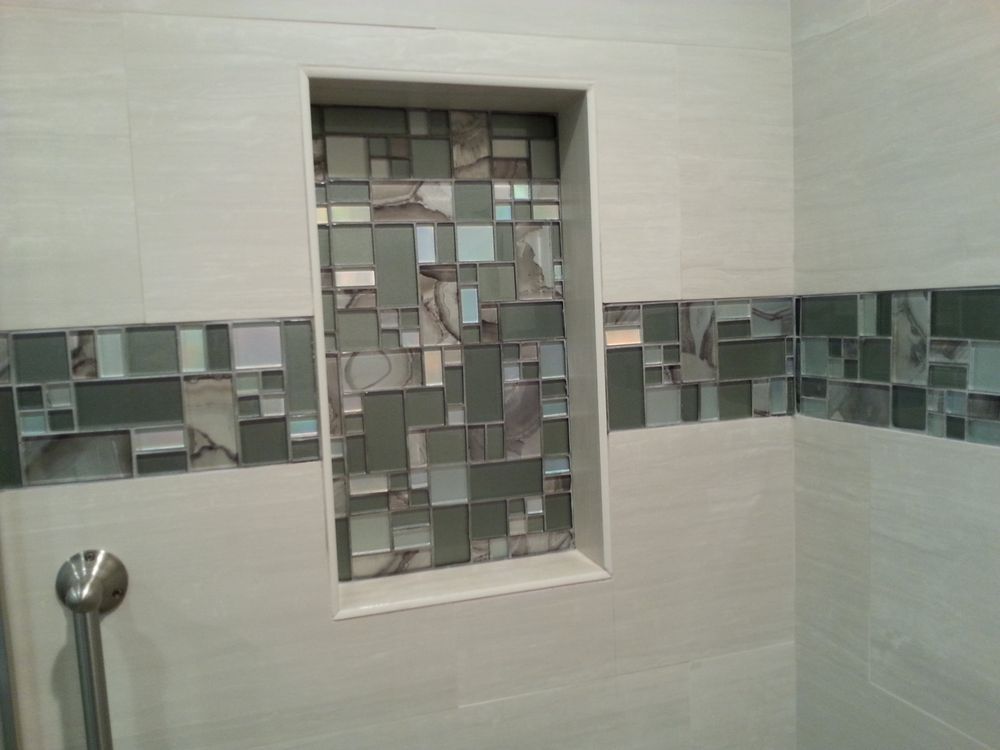 Bathroom shower wall with white tile and a mosaic glass accent niche