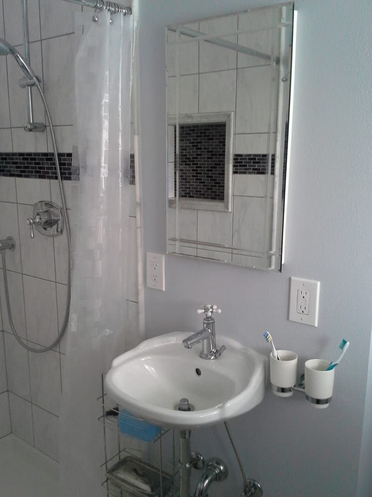 Small white bathroom with shower, sink, mirror, tiled walls, and toothbrushes on the counter.