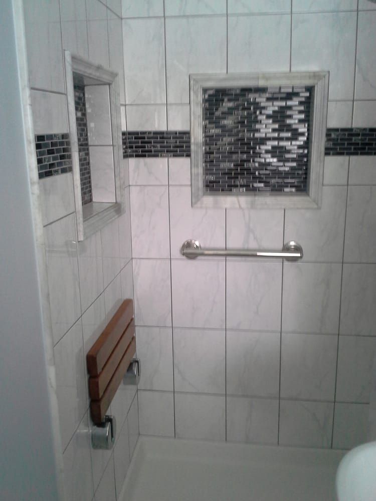 Small tiled shower with grab bars, bench seat, and frosted window.