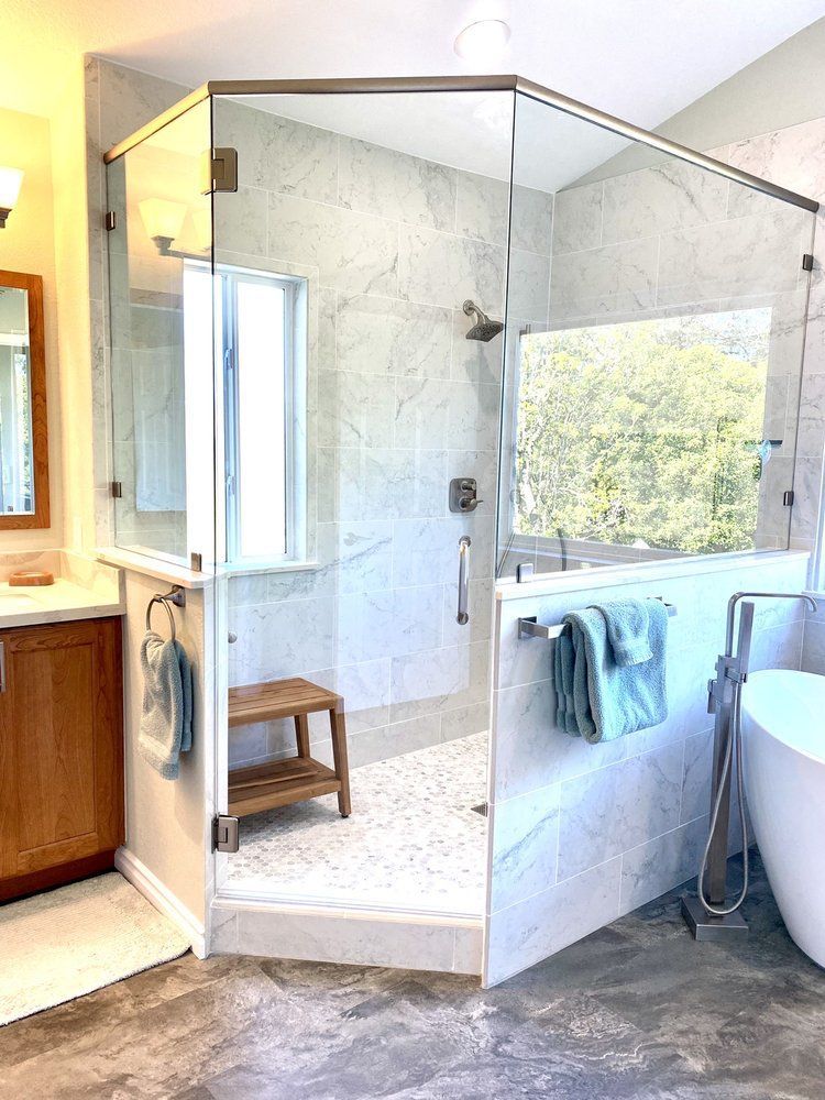 Glass-enclosed corner shower with white tile, built-in bench, and towels in a bright bathroom