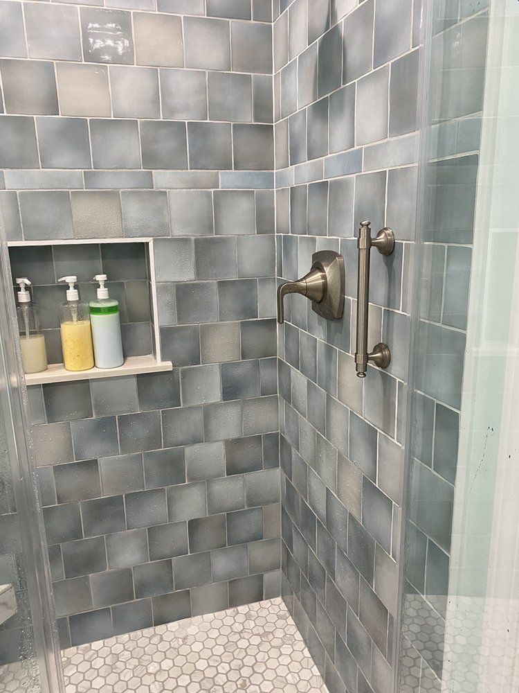 Gray-tiled shower with built-in shelf holding bottles and a glass door handle.