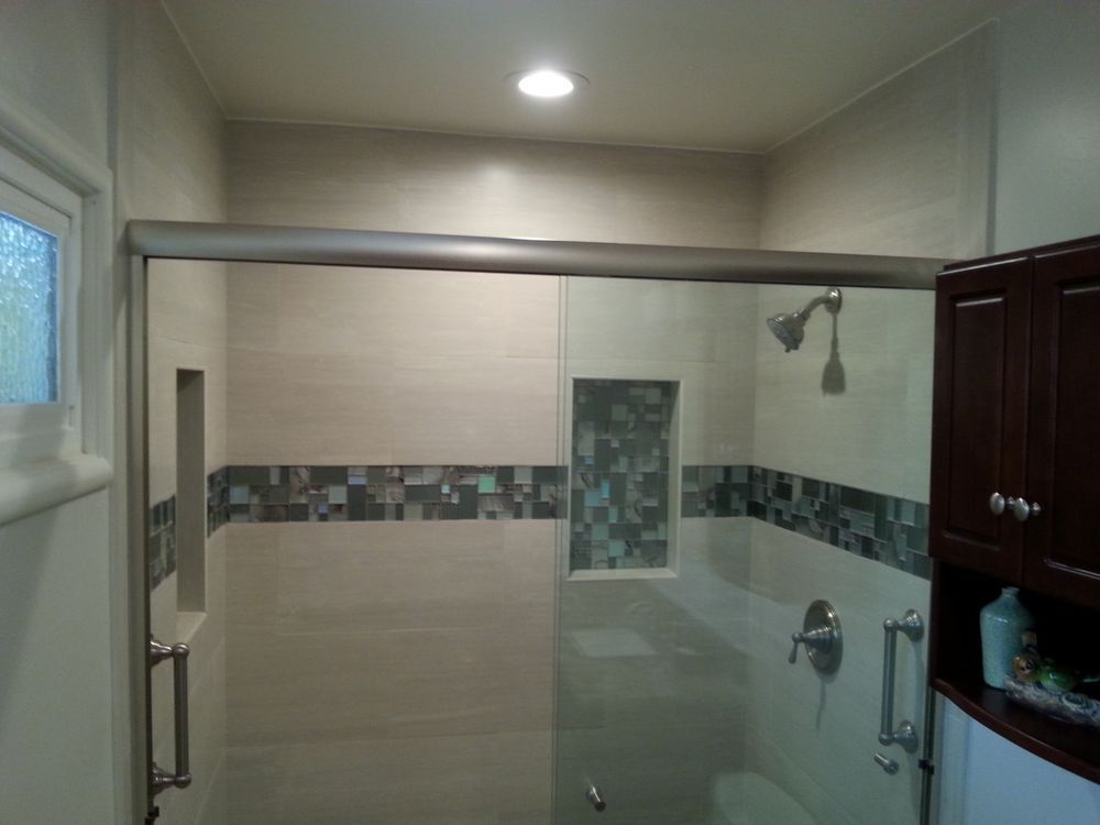 Modern bathroom with a glass shower enclosure, tiled accent strip, and dark wood vanity cabinets.