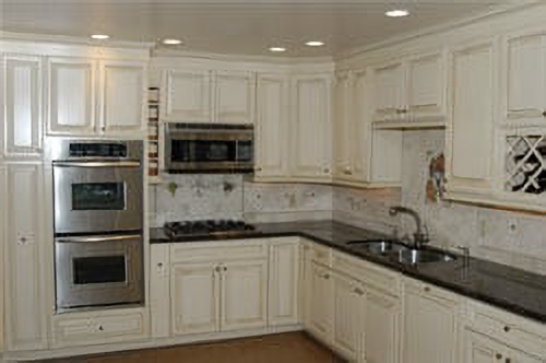 White kitchen with stainless steel appliances, black countertops, and light wood cabinets