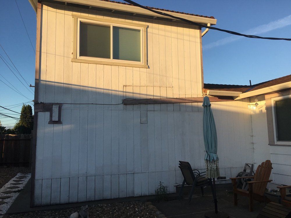 Sunlit two-story white house with a patio, chairs, and an umbrella in the yard