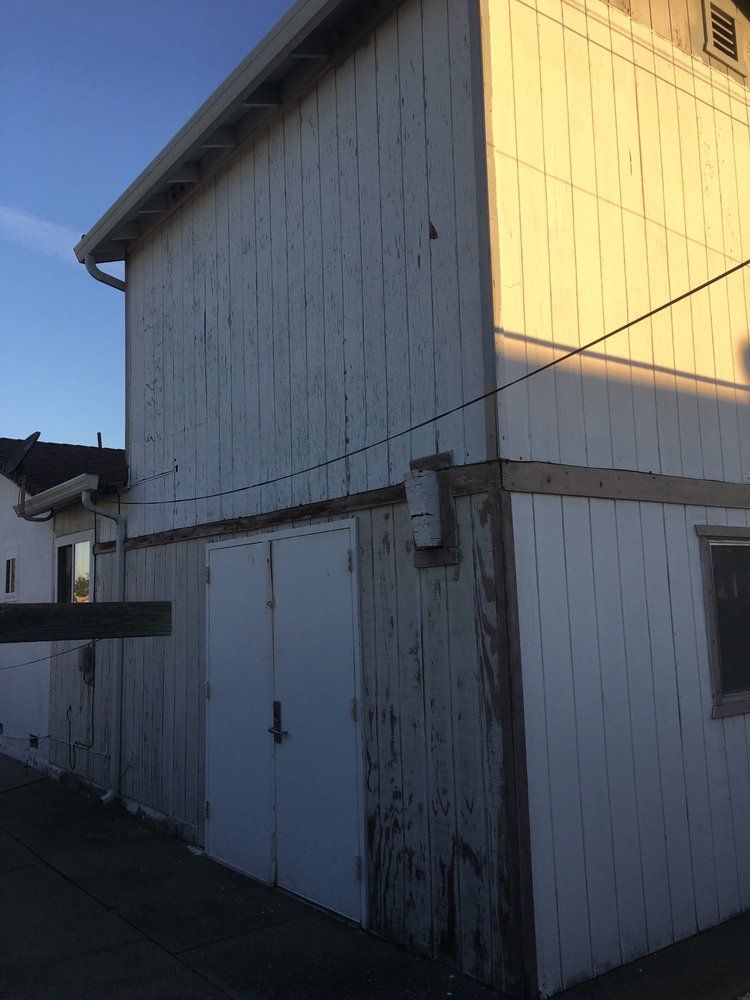 White wooden barn with double doors in sunlight against a blue sky.