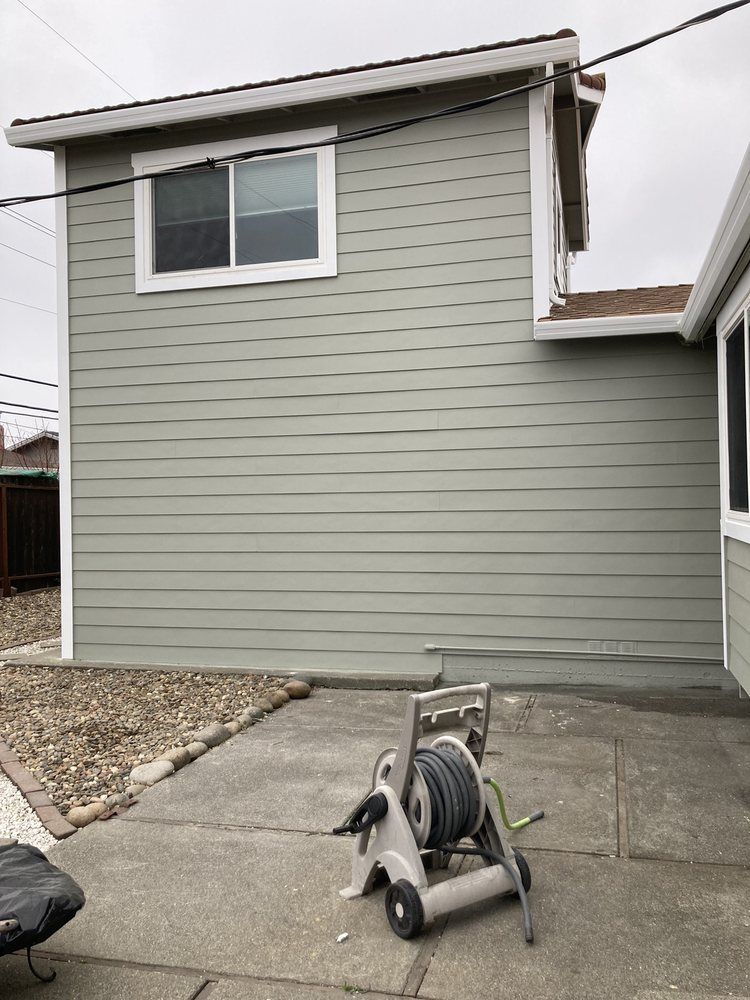 Gray house exterior with a window and patio, featuring a hose reel in the foreground.