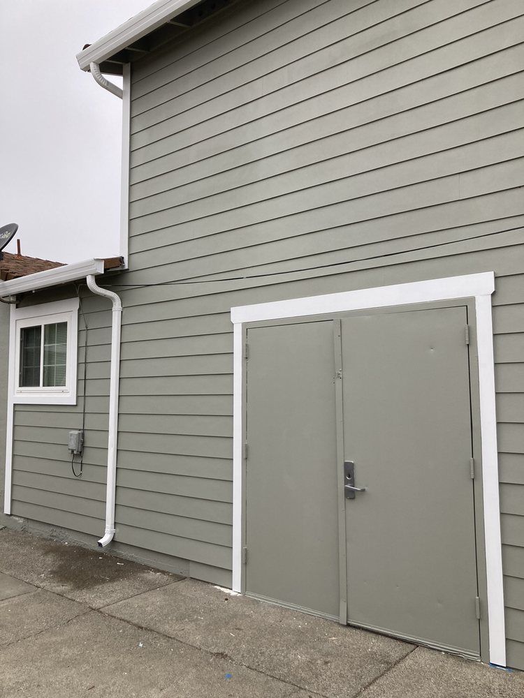 Gray building exterior with white trim and double metal doors on a concrete walkway