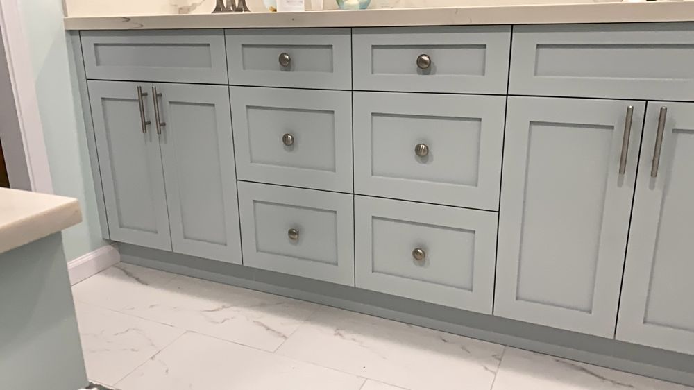 Gray bathroom vanity with multiple drawers and cabinet doors, white countertop, and marble-style tile floor