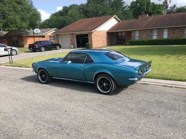 Teal classic car parked on a street in front of a suburban house.